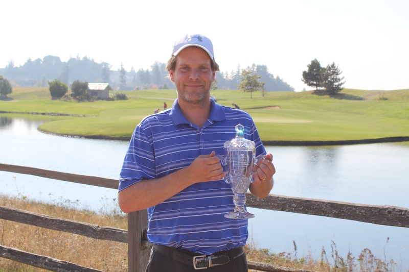 Bjorn Bjorke holding a championship trophy with a golf course and a lake in the background